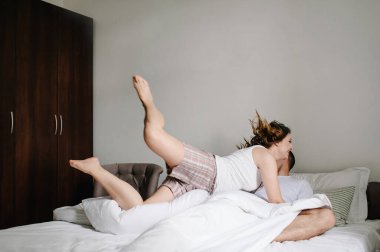 Bir kadın kocasına atlıyor. Genç yakışıklı adam yatak odasında yatakta yatıyor. Sevgililer Günü Konsepti. Birlikte vakit geçirmenin tadını çıkarıyorum. Ben de seni seviyorum. Mutluluk duyguları..