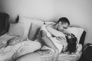 Büyük bir yatak odasında, erkek erkeğe sarılan bir kadın. Sevgililer Günü Konsepti. Yan görünüş. Aşk hikayesi. Kapatın. Mutluluk duyguları güzel genç bir çift. Yaşam tarzı. Siyah beyaz fotoğraf.