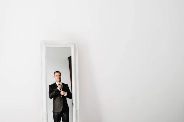 Мужчина Костюме Смотрит Свое Отражение Зеркале Выпрямляет Галстук Рубашке Дома — стоковое фото