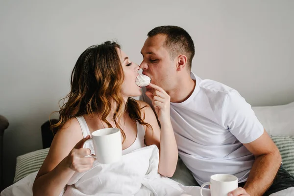 가족의 휴일에 남자와 여자가 커피를 마시고 침대나 침실에서 마시멜로를 먹습니다 — 스톡 사진