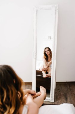 Genç seksi kız aynanın önünde oturur ve odanın arka planına bakar. Portre kadını. Tatil ve aşk kavramı.