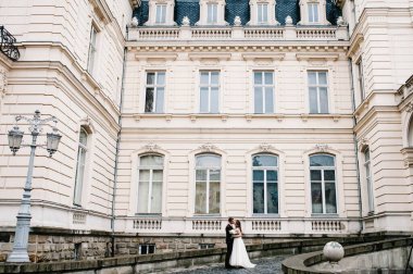 Yeni evliler ayakta duruyor ve sarılıyorlar, antik restore edilmiş mimarinin yakınında öpüşüyorlar, eski bina, eski ev dışarıda, klasik saray dışarıda..