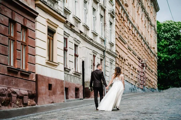 Portrait the groom and the bride walking back near old building, old house outside, outdoor. Newlyweds are walking along the streets of the city of Lviv. Wedding walks.