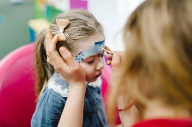 Çocuk odasında komik boyalı yüzü olan dört yaşında şirin bir kız çocuğu, bir doğum günü partisinde kapalı bir yerde. Çocuklar tatil, etkinlik, Cadılar Bayramı partisi, eğlence.