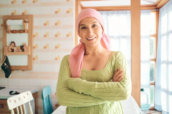 A young woman cancer survivor wearing a pink scarf, she is smiling with her arms crossed and looking at the camera