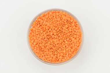 Bir kasede çiğ turuncu mercimek, beyaz arka planda üst manzara.