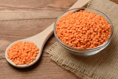 Tabakta çiğ turuncu mercimek ve tahta masada kaşık.