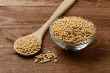 Tabakta çiğ sarı mercimek ve masada tahta kaşık.