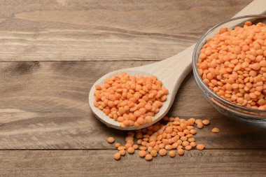 Tabakta çiğ turuncu mercimek ve tahta masada kaşık.
