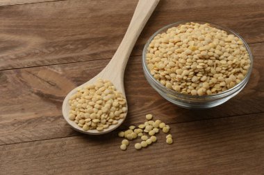 Tabakta çiğ sarı mercimek ve masada tahta kaşık.