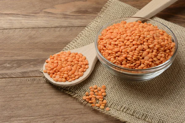 木製のテーブルの上にボウルとスプーンで生のオレンジレンズ豆 — ストック写真
