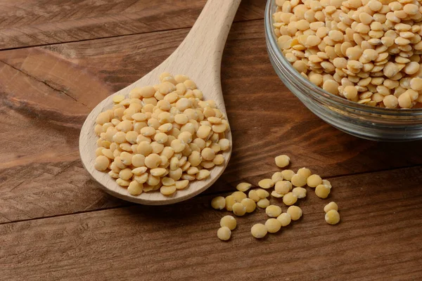 テーブルの上のボウルと木製のスプーンで生の黄色のレンズ豆 — ストック写真