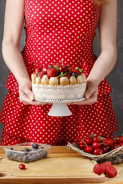 Woman holding summer sponge cake with fruits on ceramic cake sta