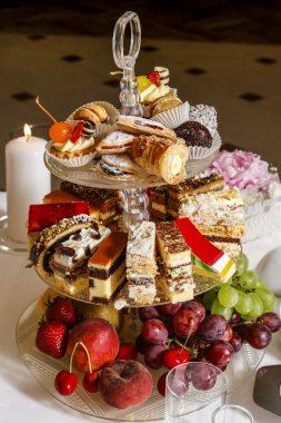 Assorted cakes, cookies and fruits on glass cake stand clipart