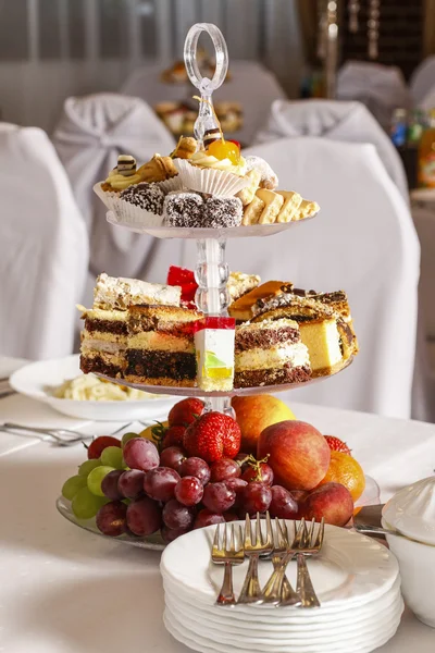 Bolos variados, biscoitos e frutas em bancada de bolo de vidro — Fotografia de Stock