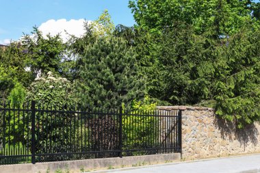 Taştan yapılmış bir çit ve diğer, sahte elementlerden yapılmış. Konutun yanındaki yemyeşil bahçe..