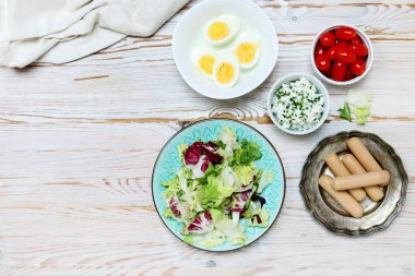 Taze salatalı kahvaltı masası, haşlanmış yumurta, kulübe, sosis ve domates. Boşluğu kopyala, tahta arkaplan.
