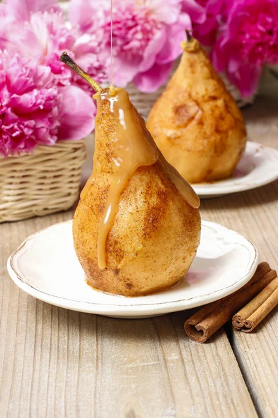Pear with caramel, beautiful pink peonies in the background — Stock Photo, Image