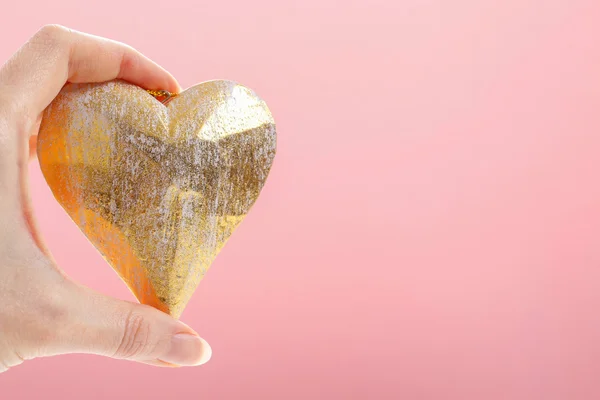 Woman holding golden heart, pink background — Stock Photo, Image