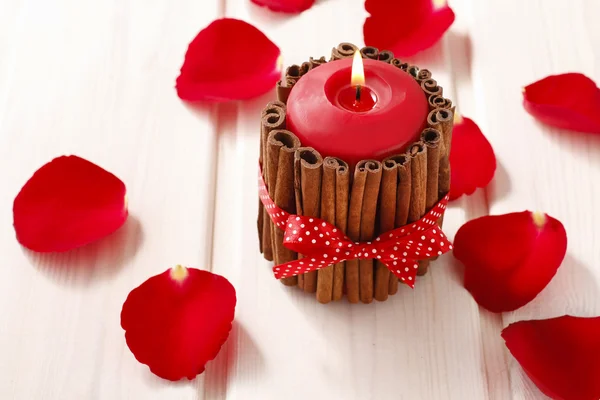 Red scented candle decorated with cinnamon sticks. Rose petals a — Stock Photo, Image