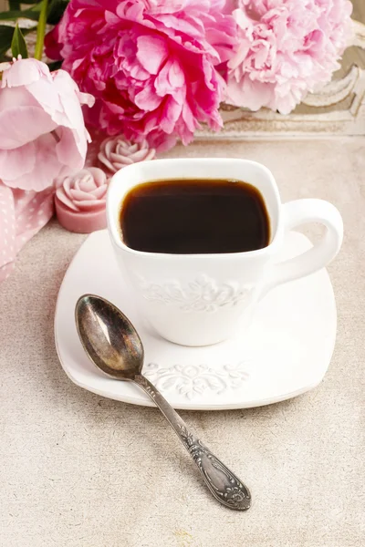 Cup of coffee and beautiful pink peonies in the background — 图库照片