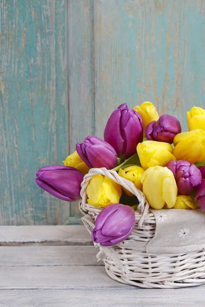 Cesta de tulipanes amarillos y violetas sobre mesa de madera —  Fotos de Stock