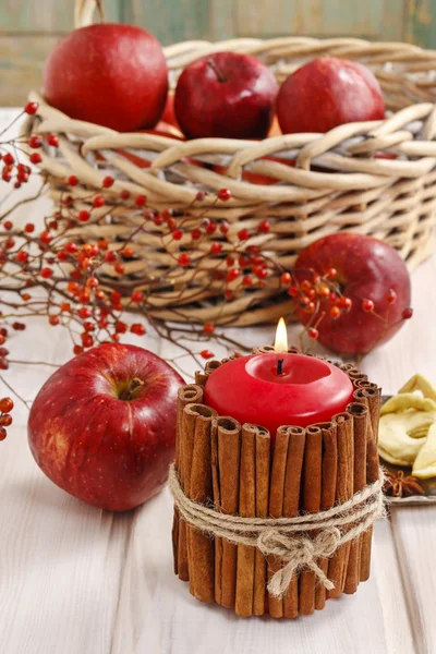 Candle decorated with cinnamon sticks and basket of apples — Stock Photo, Image