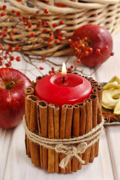 Candle decorated with cinnamon sticks and basket of apples — Stock Photo, Image