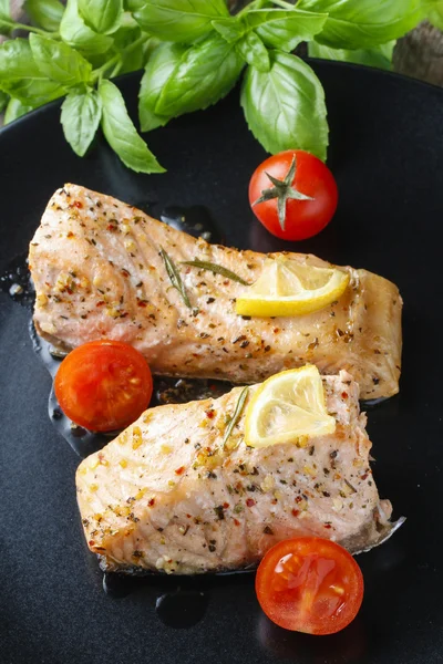 Baked salmon with herbs on the black plate — Stock Photo, Image
