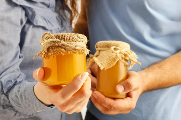 Man and woman holding glass jars of honey — Stock Photo, Image