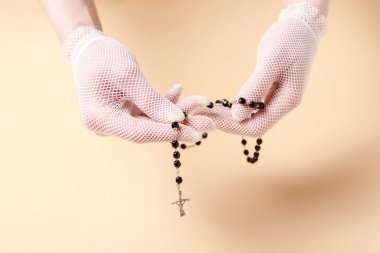 Beyaz eldivenli genç bir kadının elleri. Şeftali rengi arka planda siyah tespihi tutan eller. Grafiksel kaynaklar