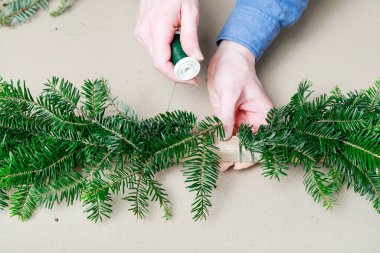 Kadın, köknar dalları, tarçın çubukları, kırmızı elmalar ve konilerle klasik Noel çelengi yapmayı gösteriyor. Adım adım, öğretici.