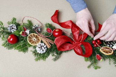 Kadın, köknar dalları, tarçın çubukları, kırmızı elmalar ve konilerle klasik Noel çelengi yapmayı gösteriyor. Adım adım, öğretici.