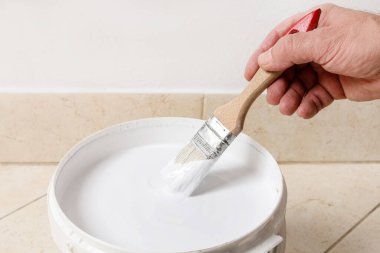 Beyaz boyalı büyük bir kova ve elinde fırça tutan bir adam. Ev ödevi