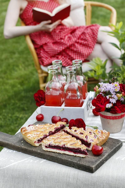 Tarte aux cerises à la table du garden party. Femme en robe rouge lecture — Photo