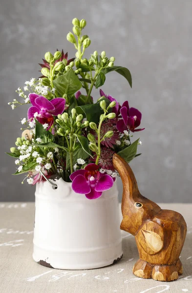 Floral arrangement with violet orchids and wooden figure of baby
