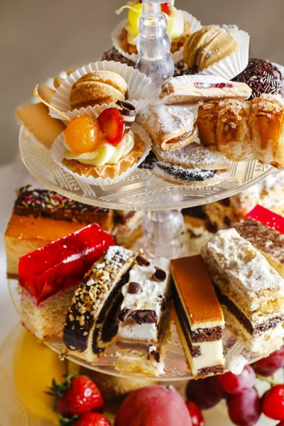 Assorted cakes, cookies and fruits on glass cake stand — Stock Photo, Image
