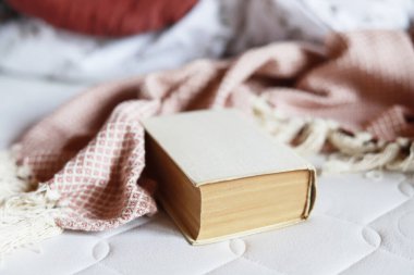 Yatağın üzerinde pembe bir battaniye ve bir kitap. Kitap okurken rahatlamak için bir metafor. Dinlenme zamanı.
