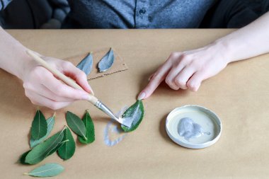 Kadın gümüş renkli yapraklara ve sonbahar meyvelerine resim yapıyor. Dekoratif fikirler. Parti dekorasyonu yapılıyor