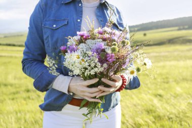 Kot ceketli genç kadın elinde çayırdan büyük, çarpıcı bir buket kır çiçeği tutuyor. Parti dekoru