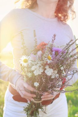 Modern elbiseli genç kadınlar çayırlardan büyük bir buket yaban çiçeği tutuyorlar. Parti dekoru
