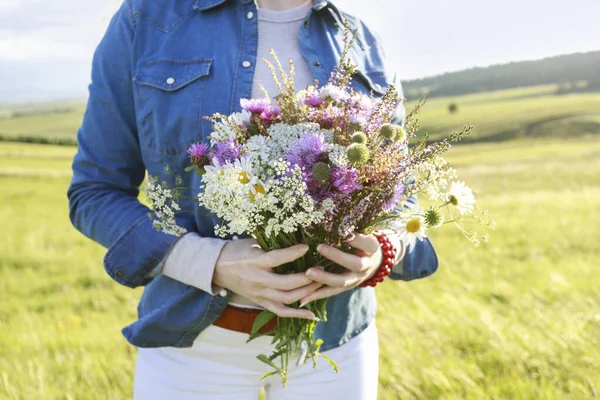 Kot ceketli genç kadın elinde çayırdan büyük, çarpıcı bir buket kır çiçeği tutuyor. Parti dekoru