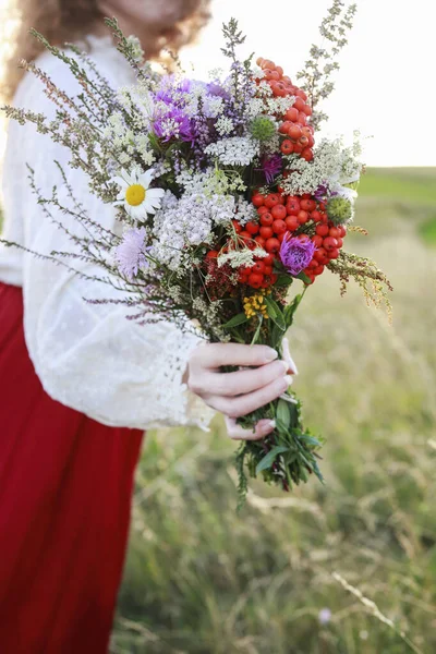 Kırmızı etekli genç bir kadın çayırdan harika bir buket yabani çiçek tutuyor. Parti dekoru