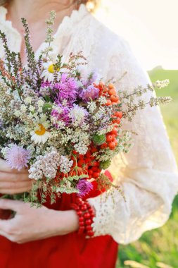 Kırmızı etekli genç bir kadın çayırdan harika bir buket yabani çiçek tutuyor. Parti dekoru