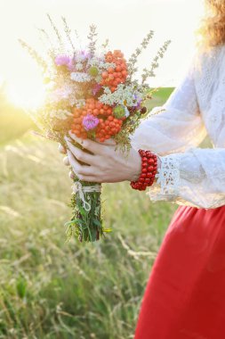 Kırmızı etekli genç bir kadın çayırdan harika bir buket yabani çiçek tutuyor. Parti dekoru
