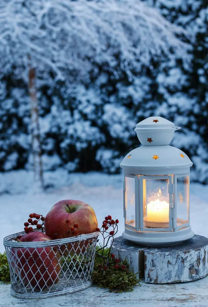 Winter evening in the garden. Iron lantern and basket of apples — Stok fotoğraf