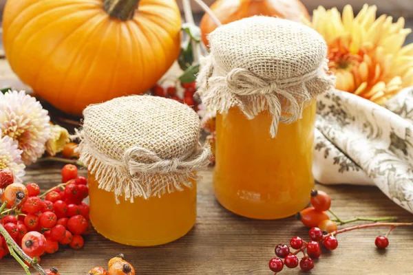 Jars of honey and beautiful autumn flowers and plants — Stock Photo, Image