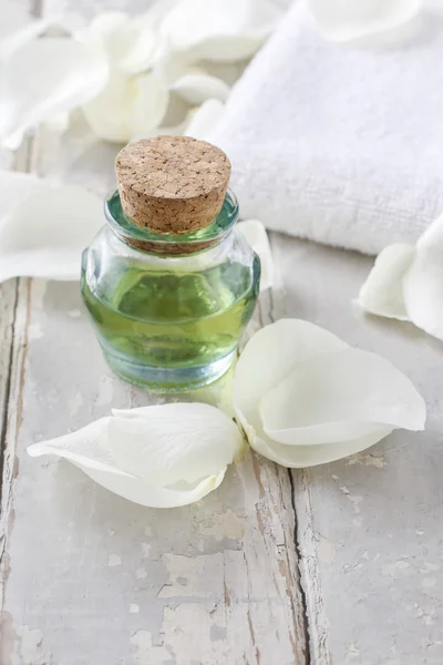 Fles van groene etherische olie, wit roze bloemblaadjes en zachte handdoek — Stockfoto