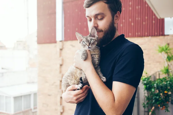 Homem bonito está segurando e abraçando seu lindo gato curioso Devon Rex — Fotografia de Stock