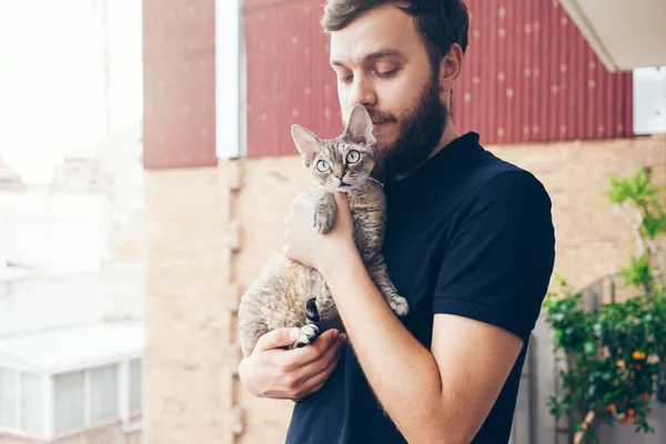  Güzel adam tutuyor ve onun sevimli meraklı Devon Rex kedi sarılma